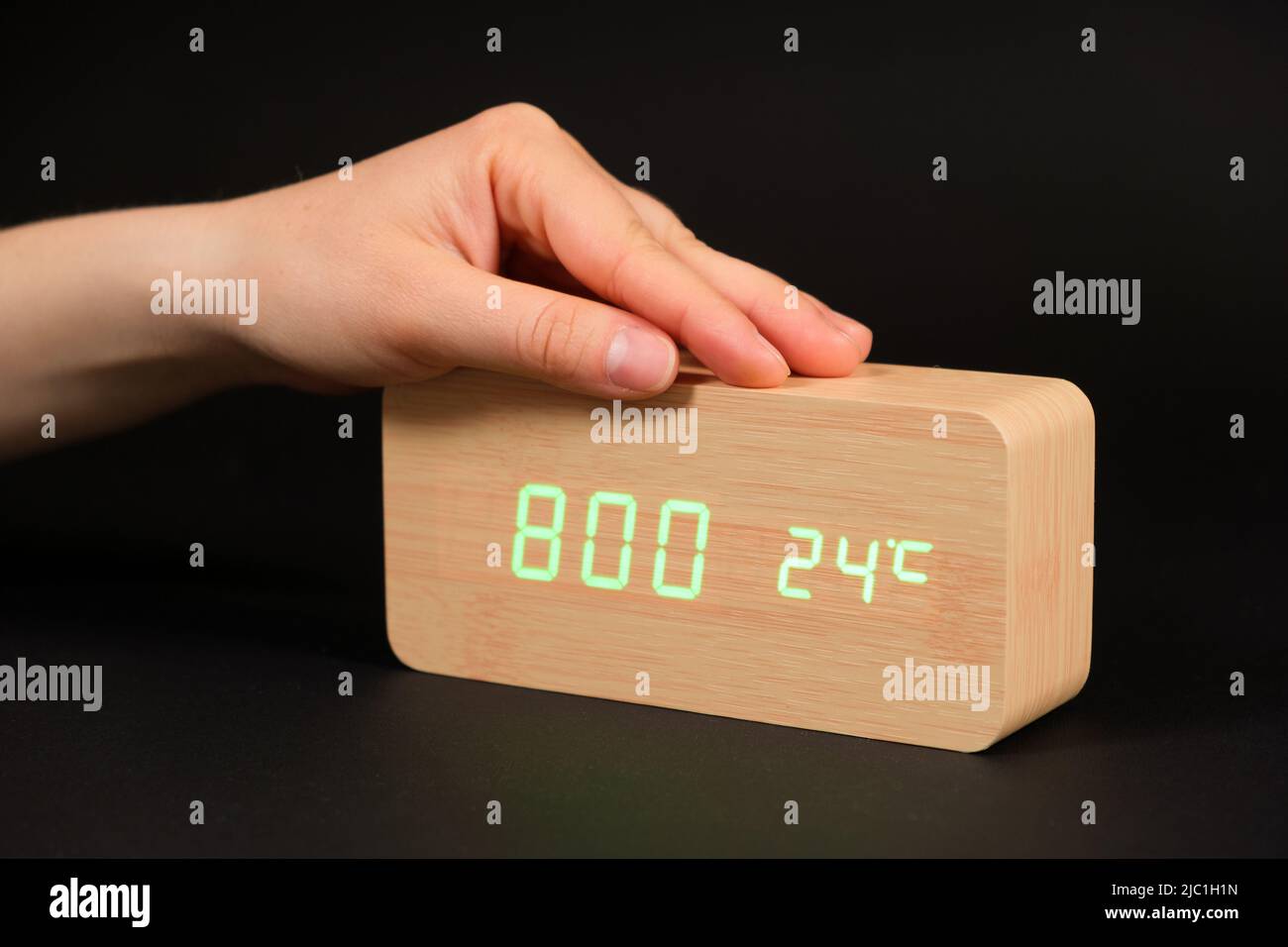 A digital clock showing a time of eight o'clock in the morning and a woman's hand on a black
