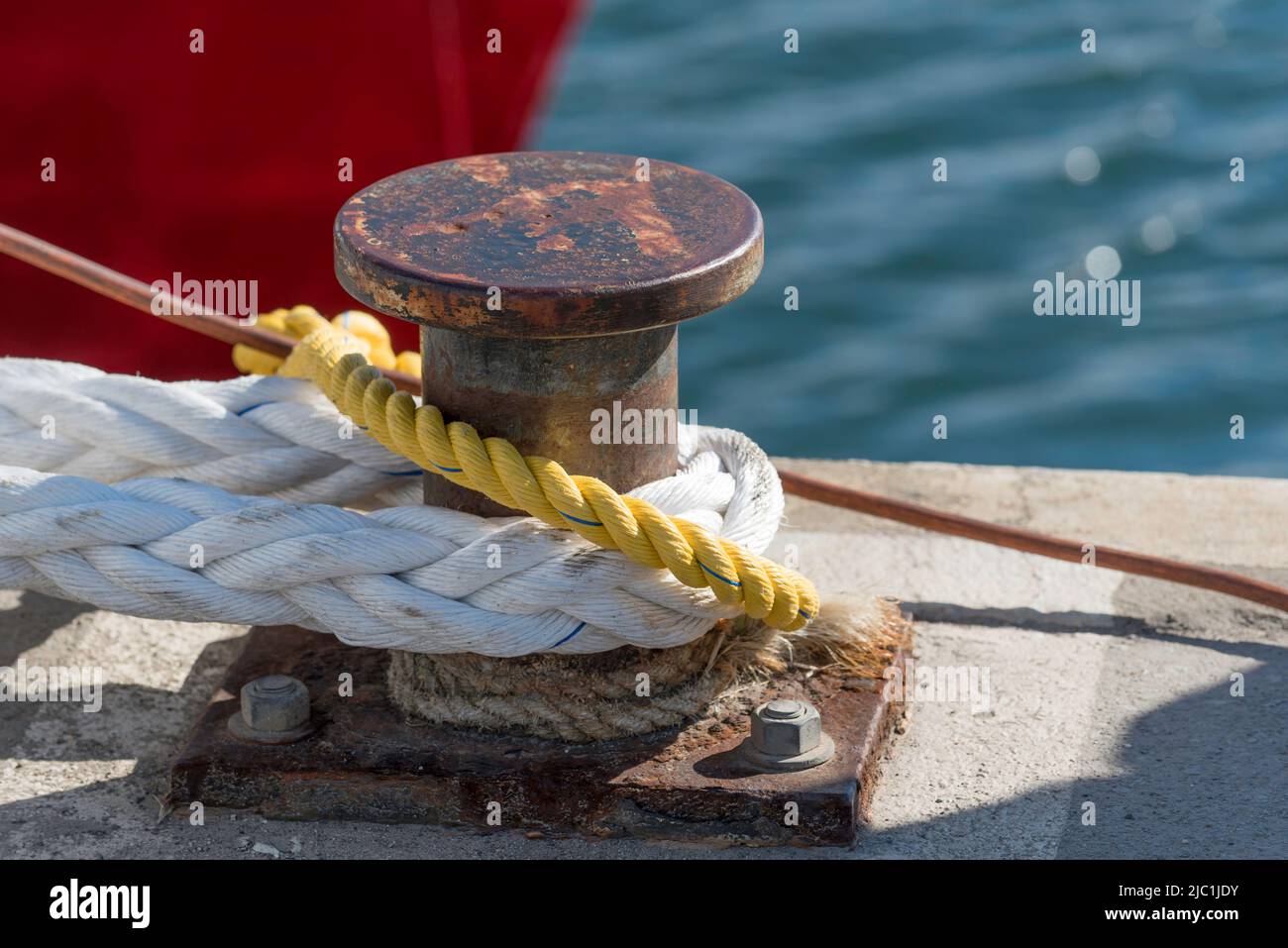 A wharf bollard in the sun with heavy nylon mooring lines attached in
