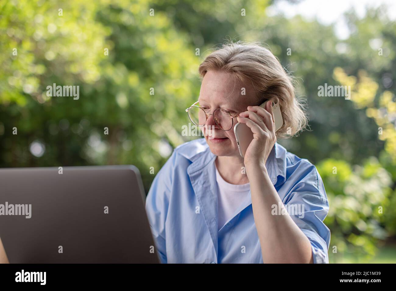 Mature adult woman working on a laptop and talking on a mobile phone Stock Photo