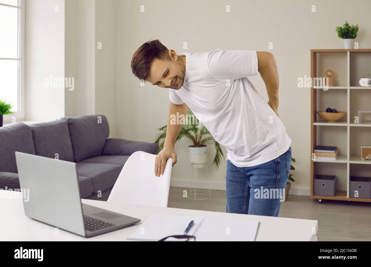 Young man gets tired and feels intense back pain after working at his computer desk Stock Photo