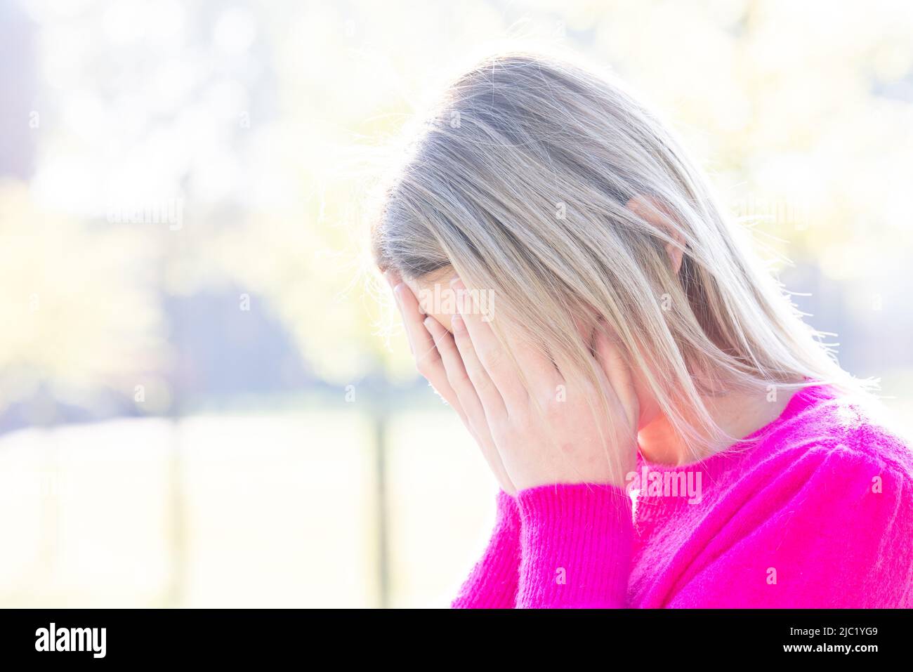 Tired, sad or depressed young beautiful blonde woman burries her face in her hands being frightened, having anxiety attack or headache migraine or depression, upset frustrated girl troubled with problem feel stressed cover crying face with hand suffer from grief sorrow concept. High quality photo Stock Photo