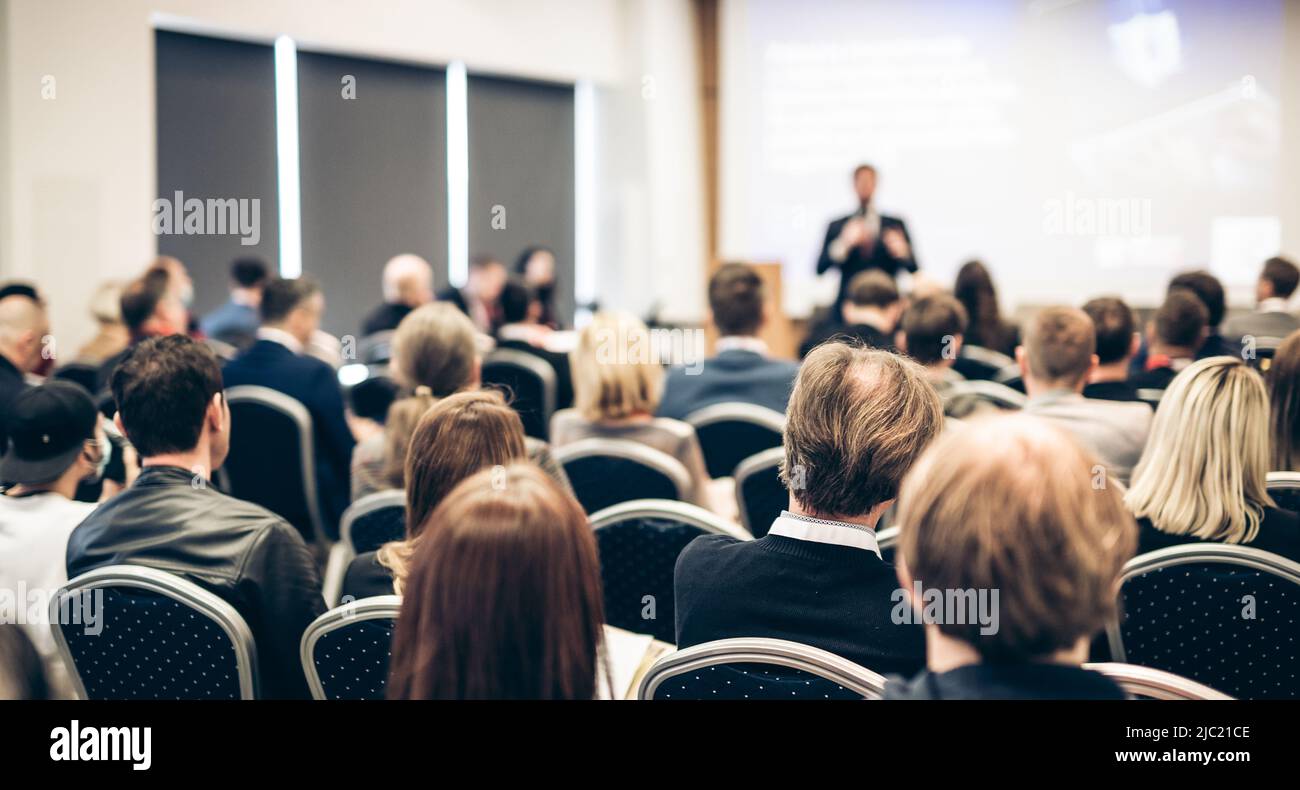 Speaker giving a talk in conference hall at business event. Rear view of unrecognizable people in audience at the conference hall. Business and Stock Photo