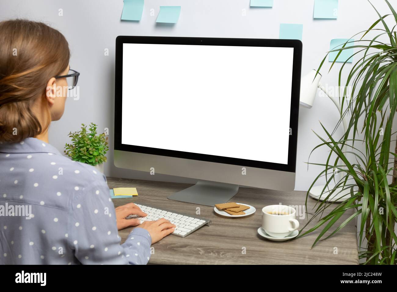 A woman is working on a desktop with a computer with a white blank screen. Mockup concept. Stock Photo