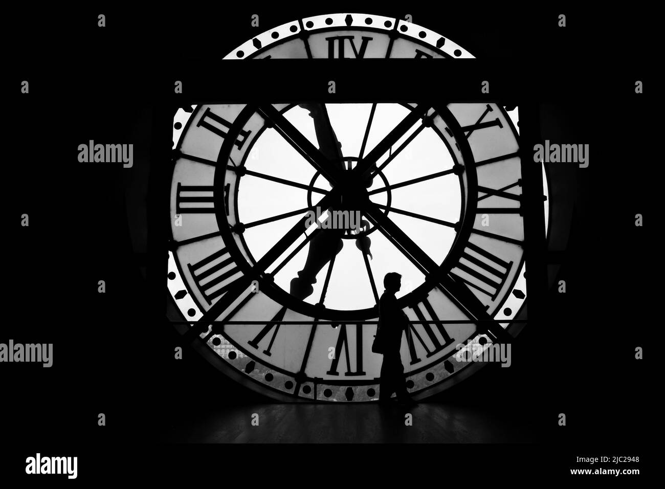 Paris, France: dramatic black and white silhouette of a woman standing still as the hands of time move along. Large clock face in the Musee d'Orsay. Stock Photo