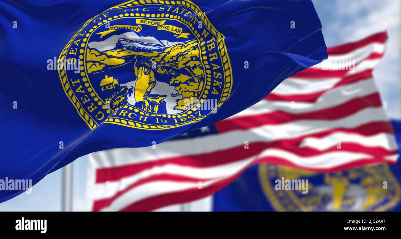 The Nebraska state flag waving along with the national flag of the United States of America. In the background there is a clear sky. Nebraska is a sta Stock Photo