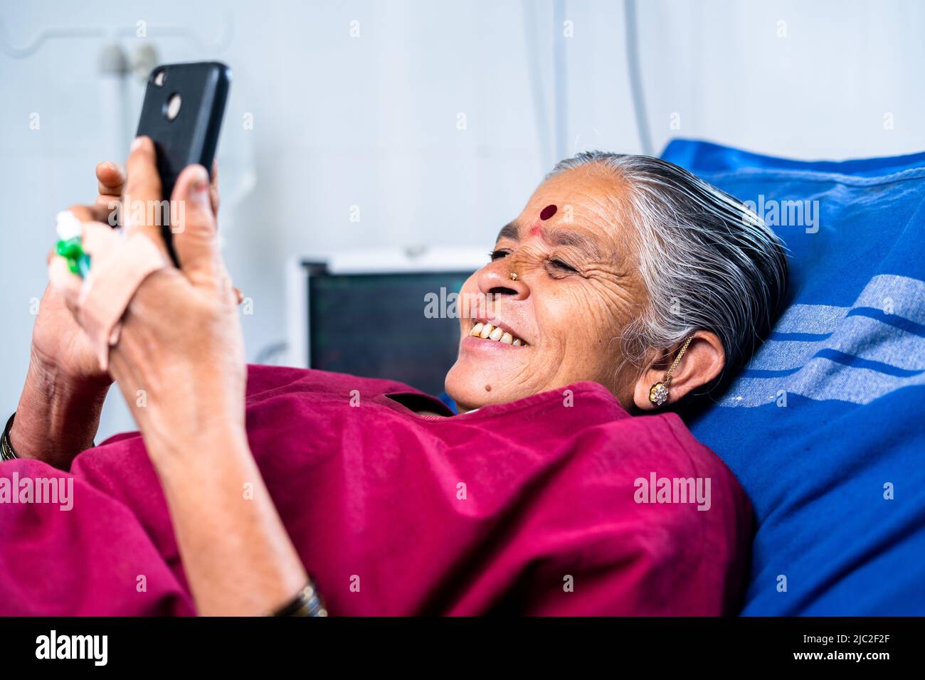 happy smiling sick woman using mobile phone at hospital while sleeping on bed - concept of technology, social media, treatment and healthcare Stock Photo