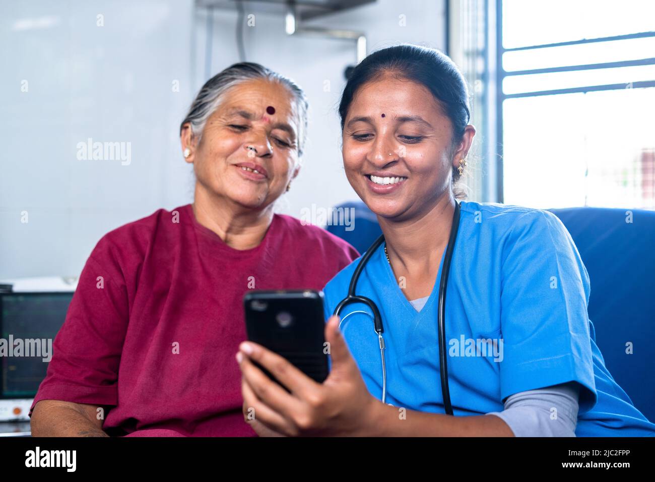 focus on nurse happy smiling sick senior woman with nurse laughing by watching mobile phone at hospital - concept of technology, relaxation and Stock Photo