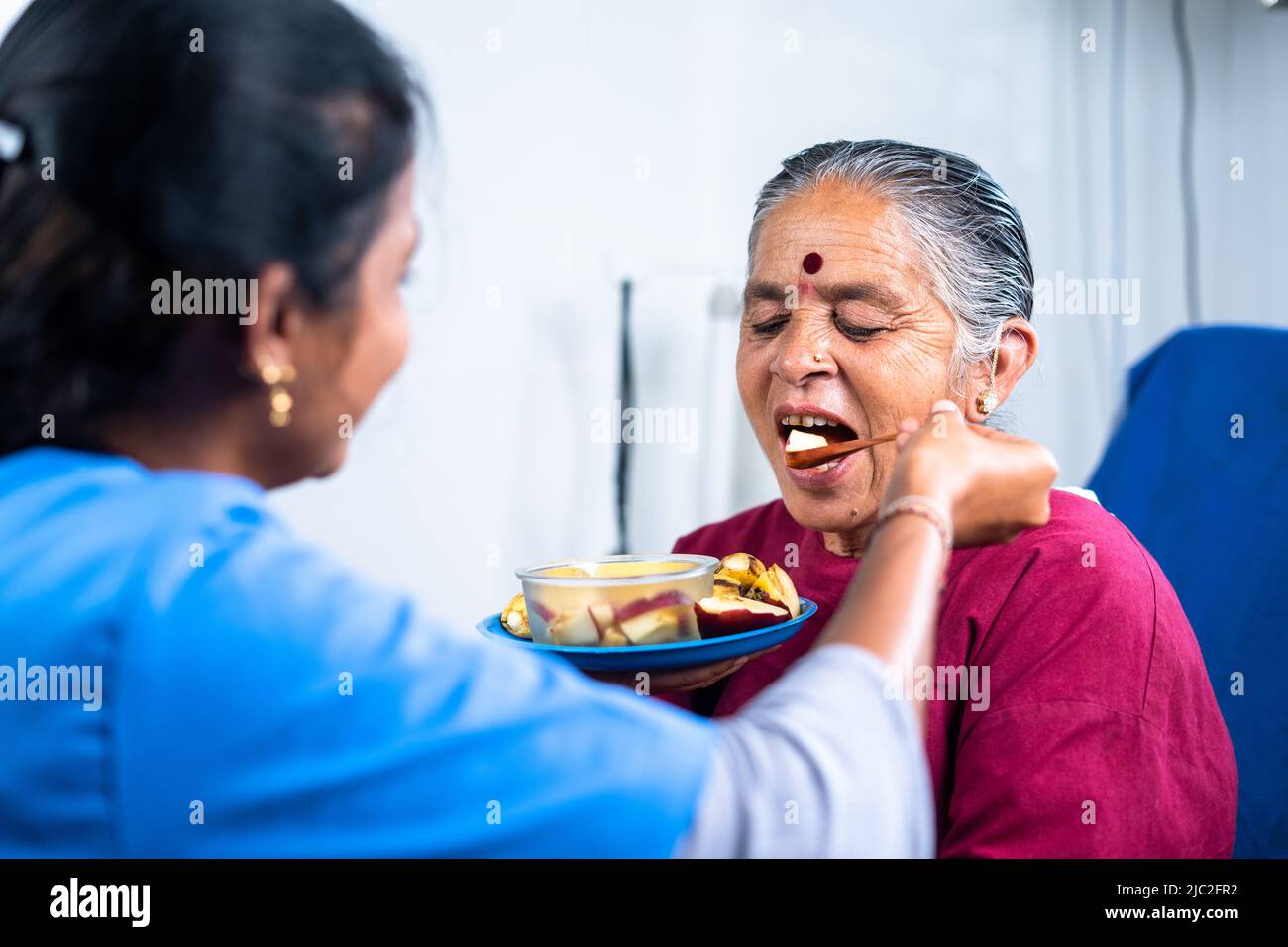 Nurse helping sick senior women to eat fruits at hospital - concept of healthcare, medicare and caretaker Stock Photo