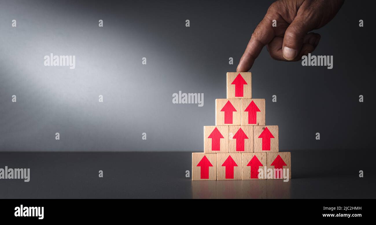 concept of mounting inflation and the cost of living . arrows pointing up on wooden blocks with hand on grey blue background . Stock Photo
