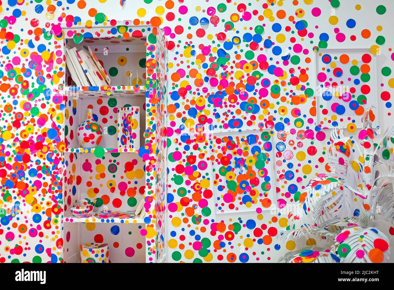 Sharjah, UAE: inside Yayoi Kusama's quirky Obliteration Room. White wall with frames and a bookshelf transformed by visitors with colorful polka dots. Stock Photo