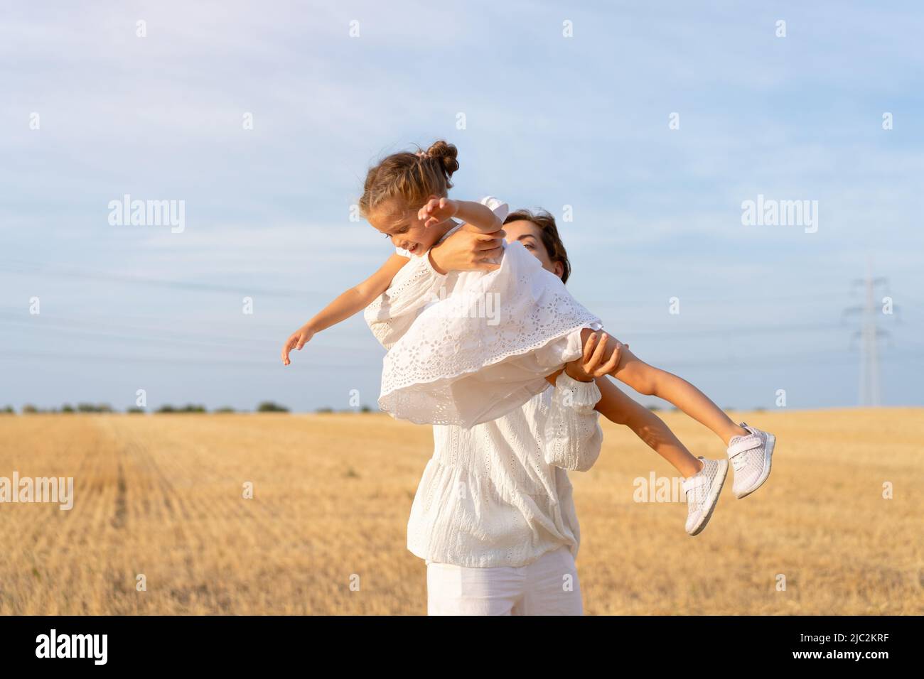 Mother throws up little daughter in air standing wheat field summer day