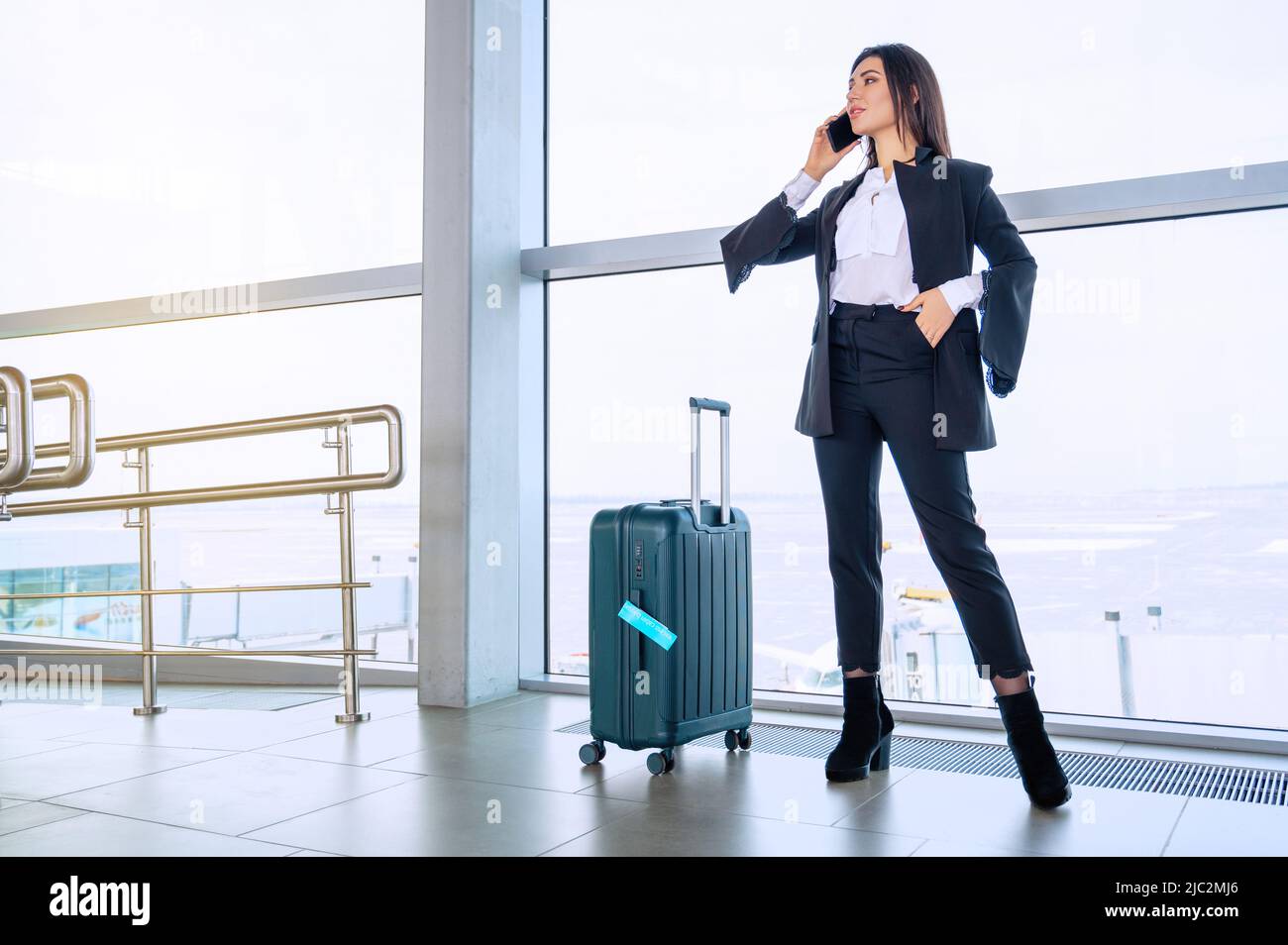 Woman with luggage waiting for flight at airport terminal in front of