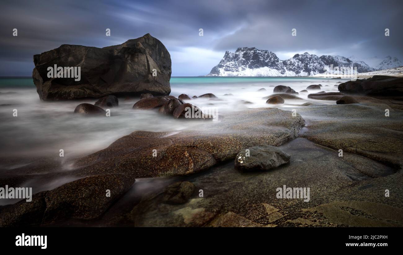 Uttakleiv rocky coast with mountains in background at cloudy sunset, Lofoten, Norway Stock Photo