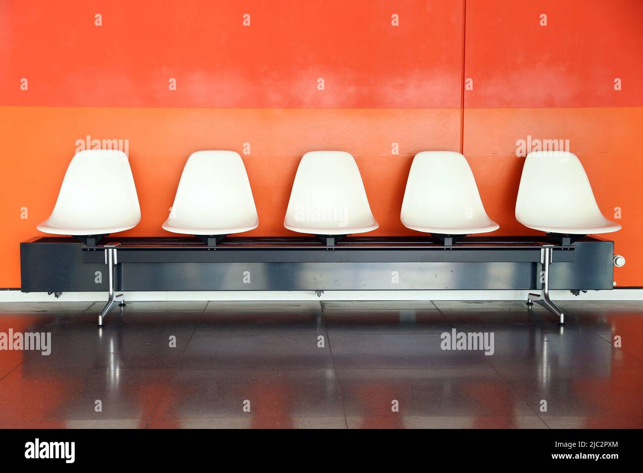 Five white plastic chairs in front of a red wall Stock Photo