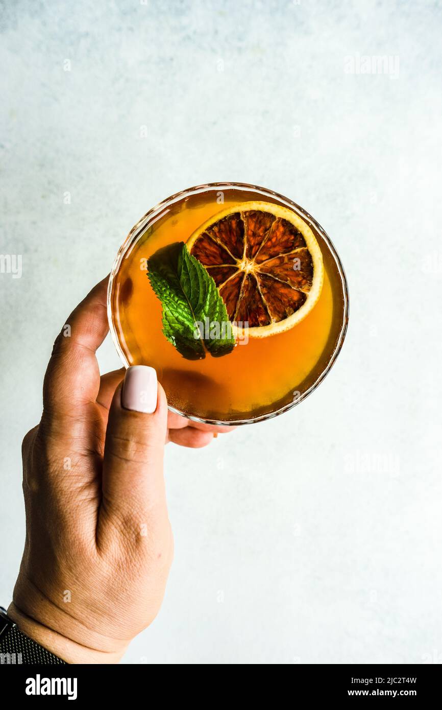 Overhead view of a woman reaching for a cocktail with a slice of orange and fresh mint Stock Photo