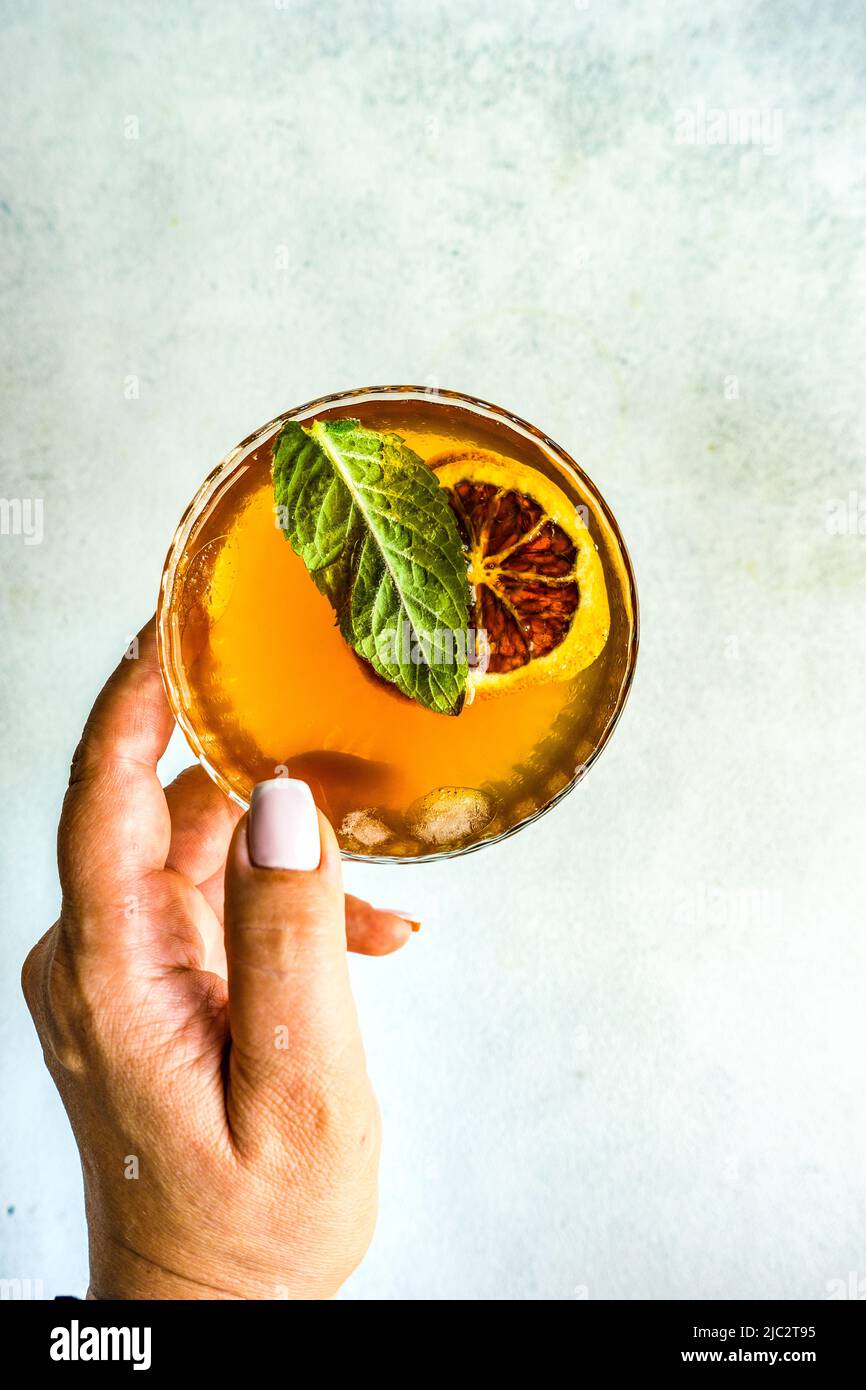 Overhead view of a woman reaching for a cocktail with a slice of orange and fresh mint Stock Photo