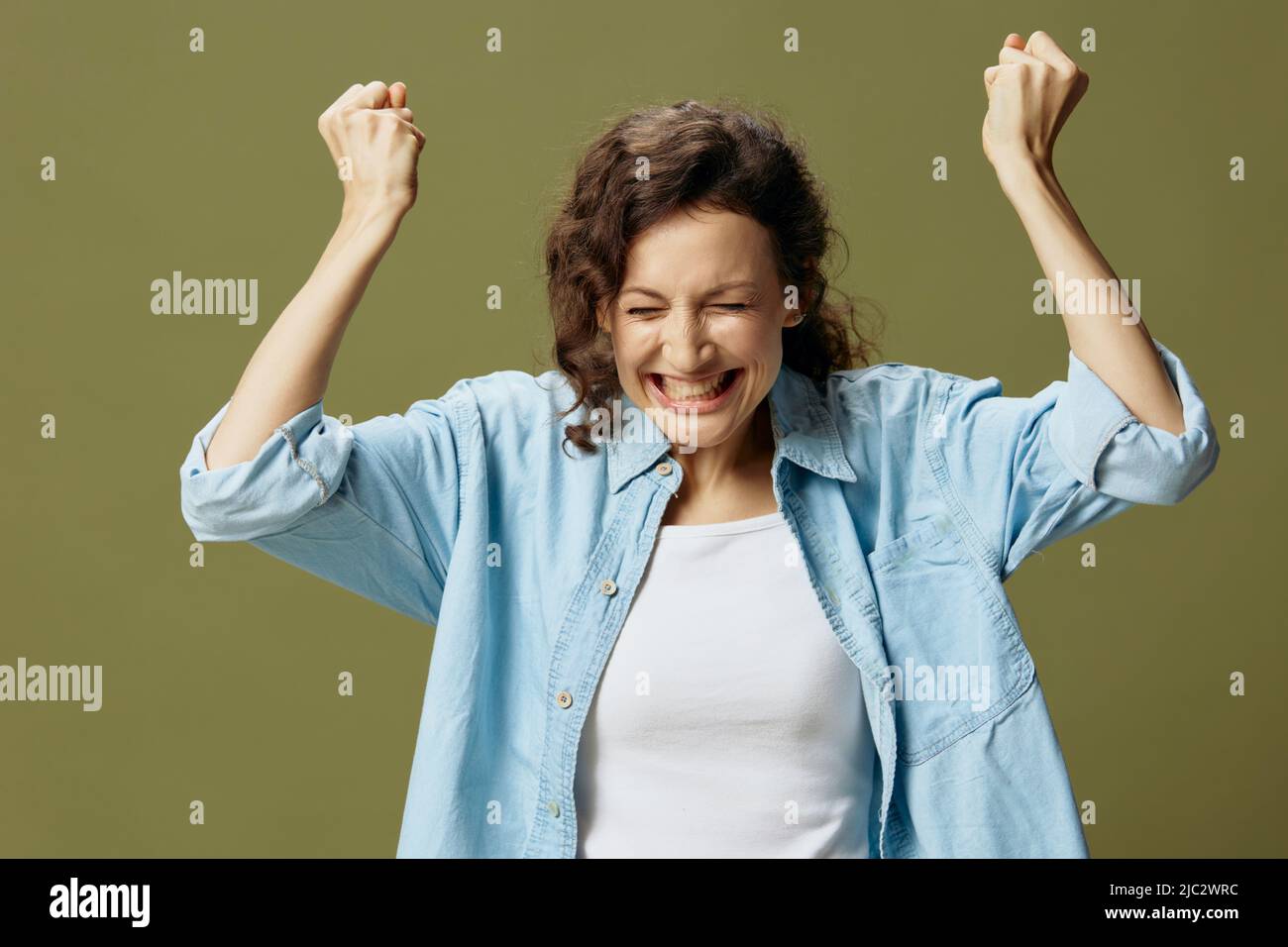 Overjoyed excited happy curly pretty lady in jeans casual shirt raise ...