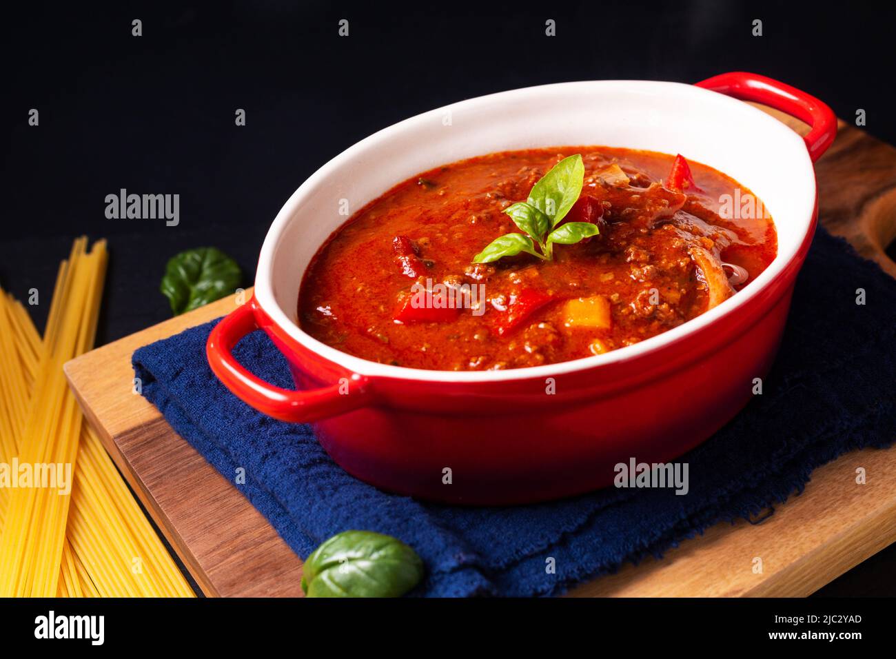 Food concept homemade italian Bolognese sauce in red oven Casseroles on wooden board with black copy space Stock Photo