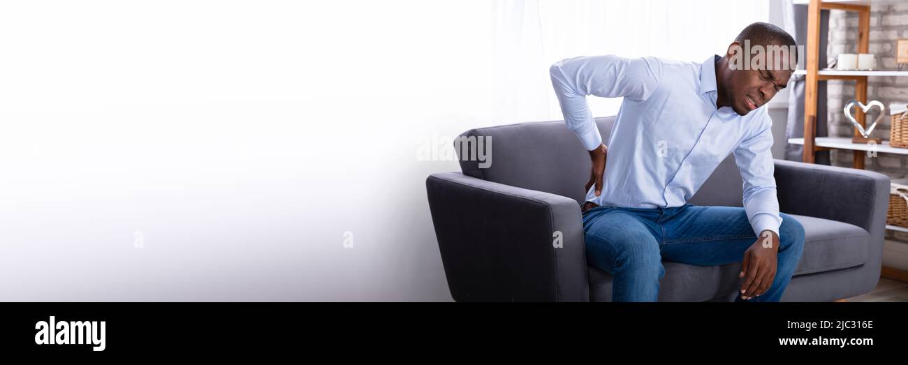 Young African Man Sitting On Sofa Having Back Pain Stock Photo - Alamy