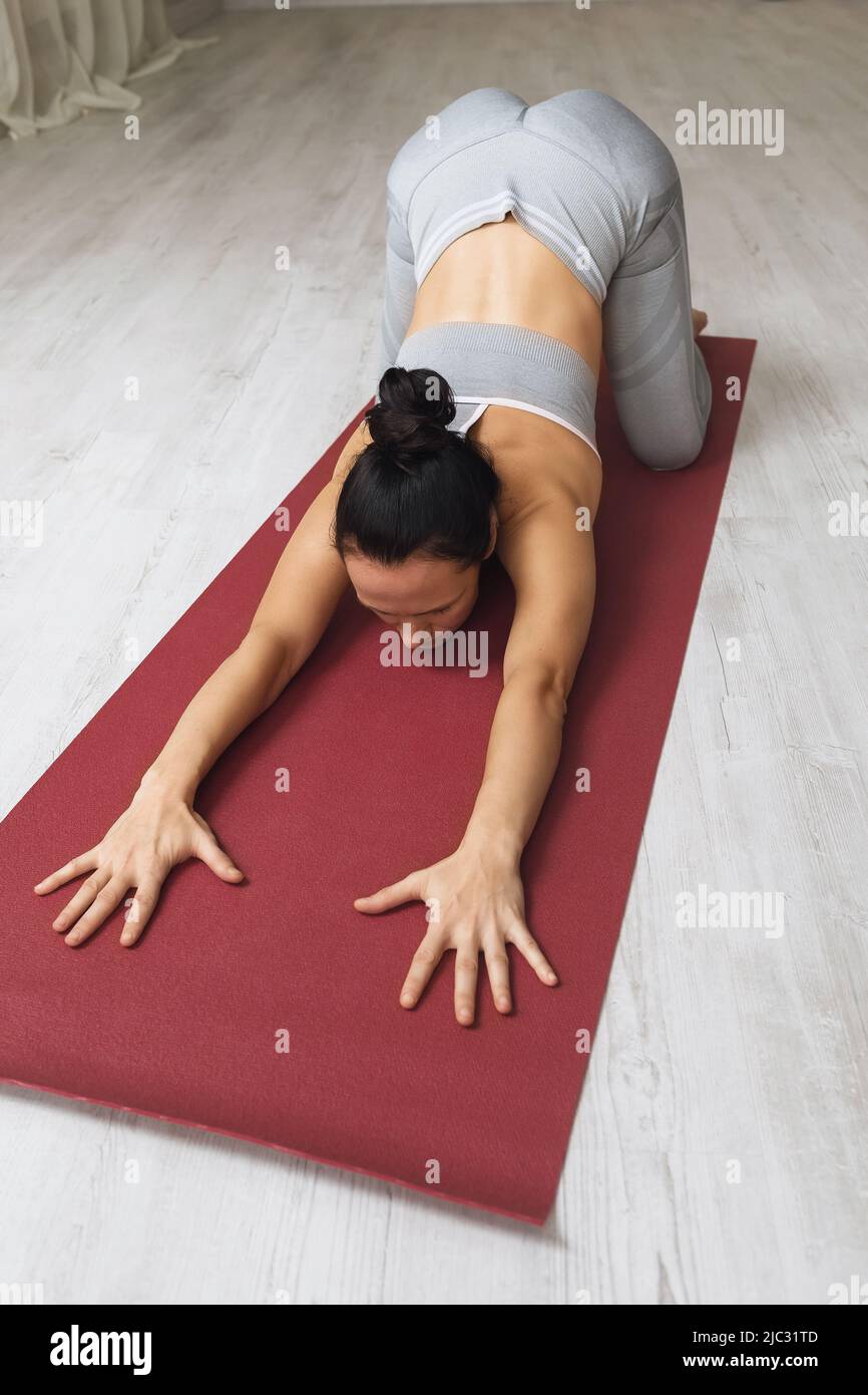 A woman practicing yoga performs a balasana exercise with an average opening of the hips, a pose of a child, she trains on a mat in the studio Stock Photo
