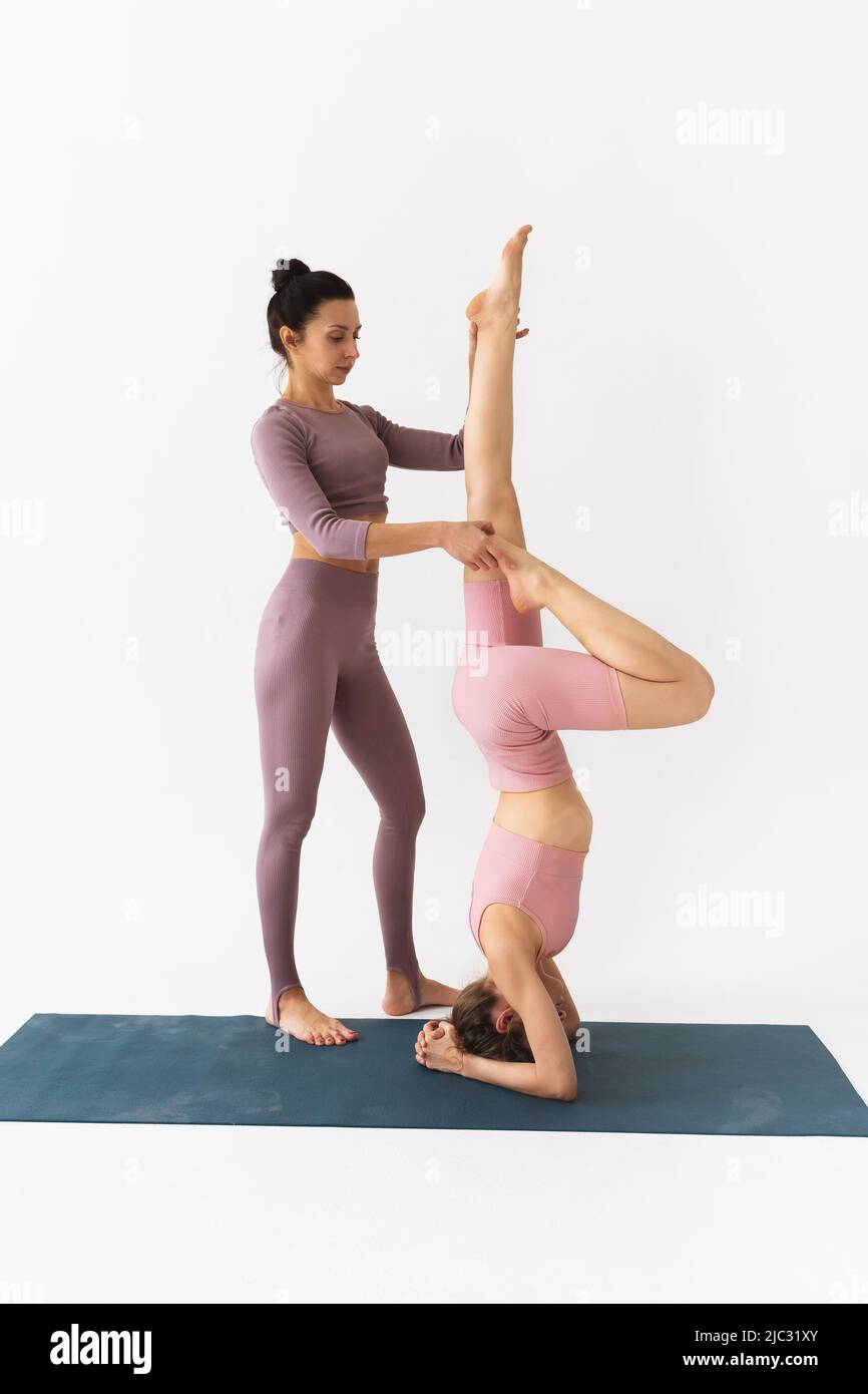 A female trainer helps a student to perform the Shirshasana exercise, an inverted asana Stock Photo