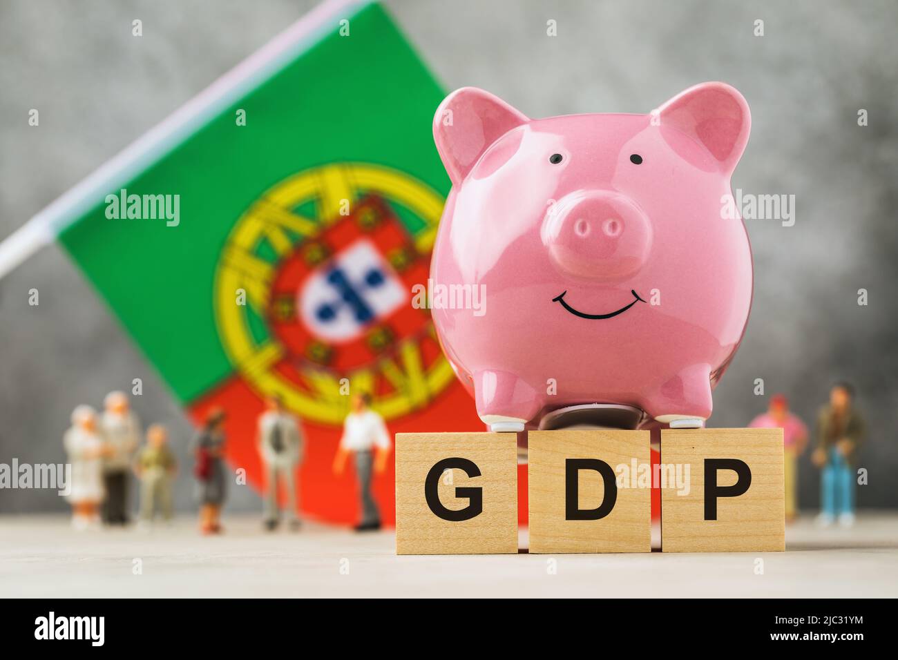 Piggy bank, wooden cubes with text, toy people made of plastic and a flag on an abstract background, a concept on the theme of Portugal GDP Stock Photo