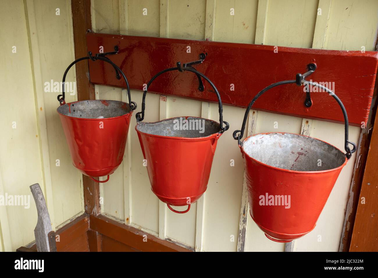 Three traditional fire buckets hanging on a wall at Bolton Abbey railway station, Yorkshire, UK Stock Photo