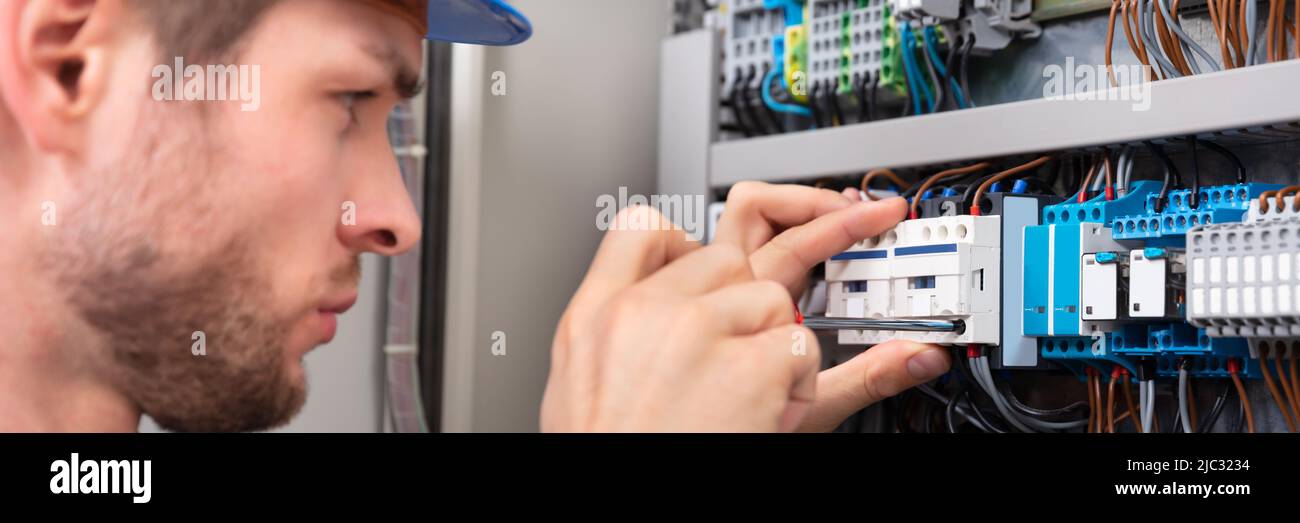 Side View Of Young Technician Repairing Fuse Box With Screwdriver Stock Photo