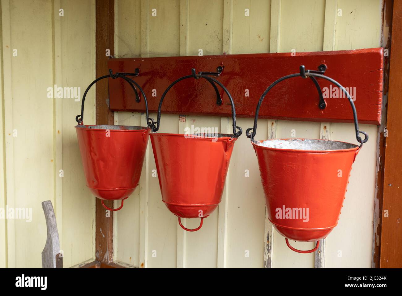 Three traditional fire buckets hanging on a wooden yellow wall at Bolton Abbey railway station, Yorkshire, UK Stock Photo