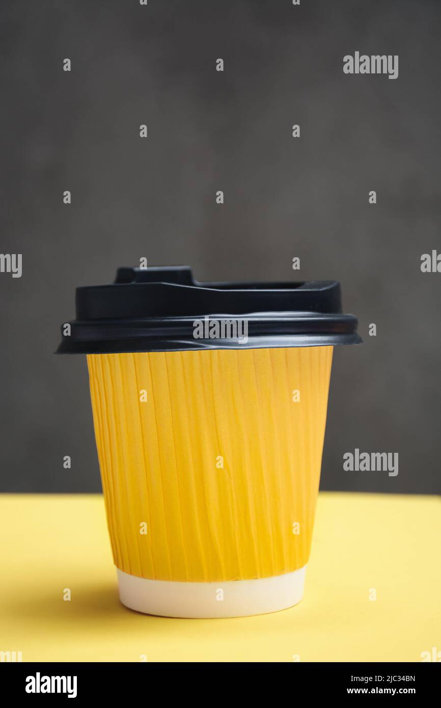 Yellow paper cup with takeaway coffee. Container on a yellow and dark