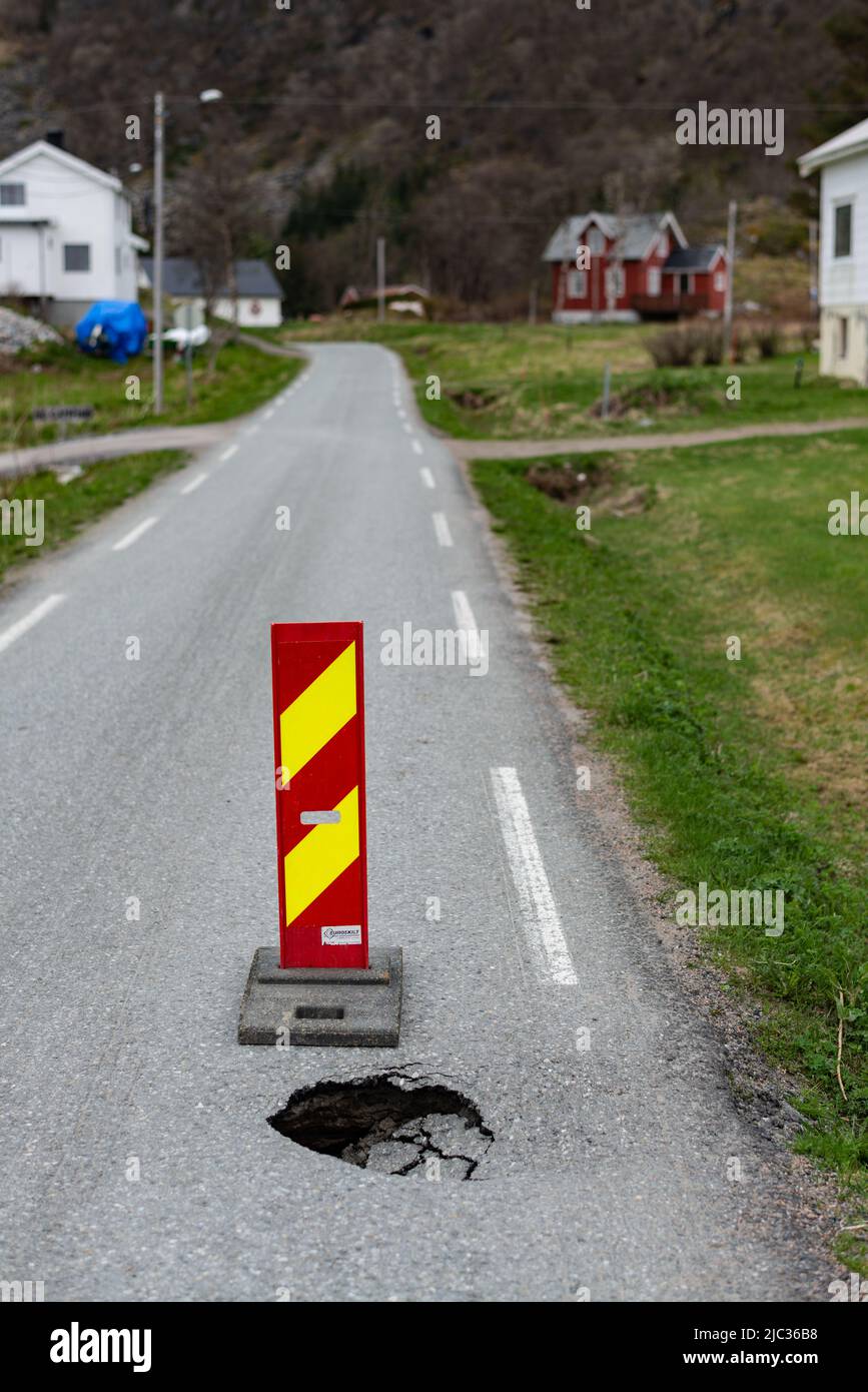 A deep hole in a narrow road, marked with a danger sign. Bøvær, Troms, Northern Norway. Stock Photo