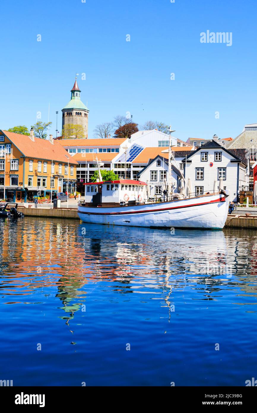 Traditional Norwegian fishing boat moored in Stavanger harbour. Old quayside warehouses are now trendy restaurants, bars and cafes., Norway. In the ba Stock Photo