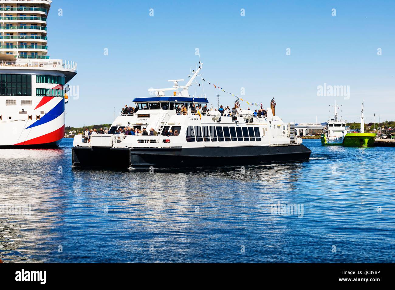 Coastal high speed catamaran passenger ferry,Teisten, enters the harbour in Stavanger, Norway. P & O Cruises MS Iona berthed at the quayside Stock Photo