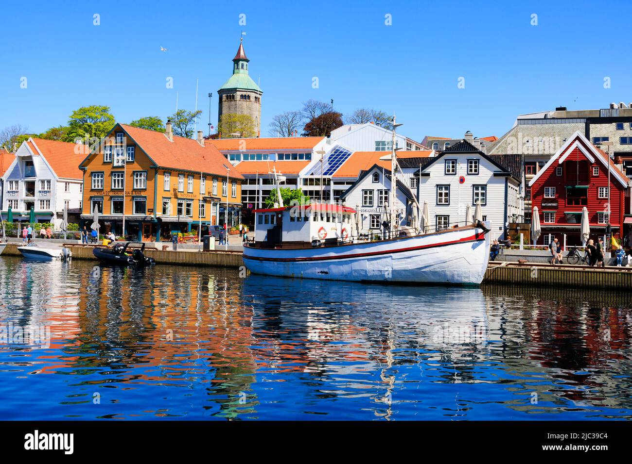 Traditional Norwegian fishing boat moored in Stavanger harbour. Old quayside warehouses are now trendy restaurants, bars and cafes., Norway. In the ba Stock Photo