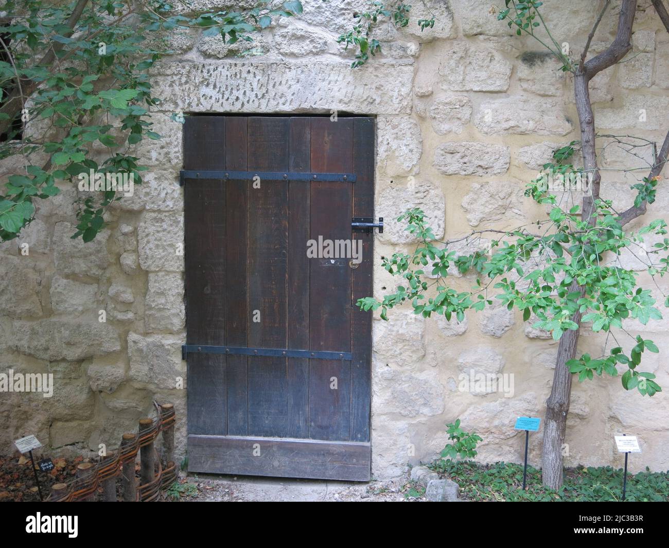 An old wooden doorway in a stone wall - leading to a secret garden?  The Jardin Medieval at Uzes in France, set in the grounds of Raynon Castle. Stock Photo