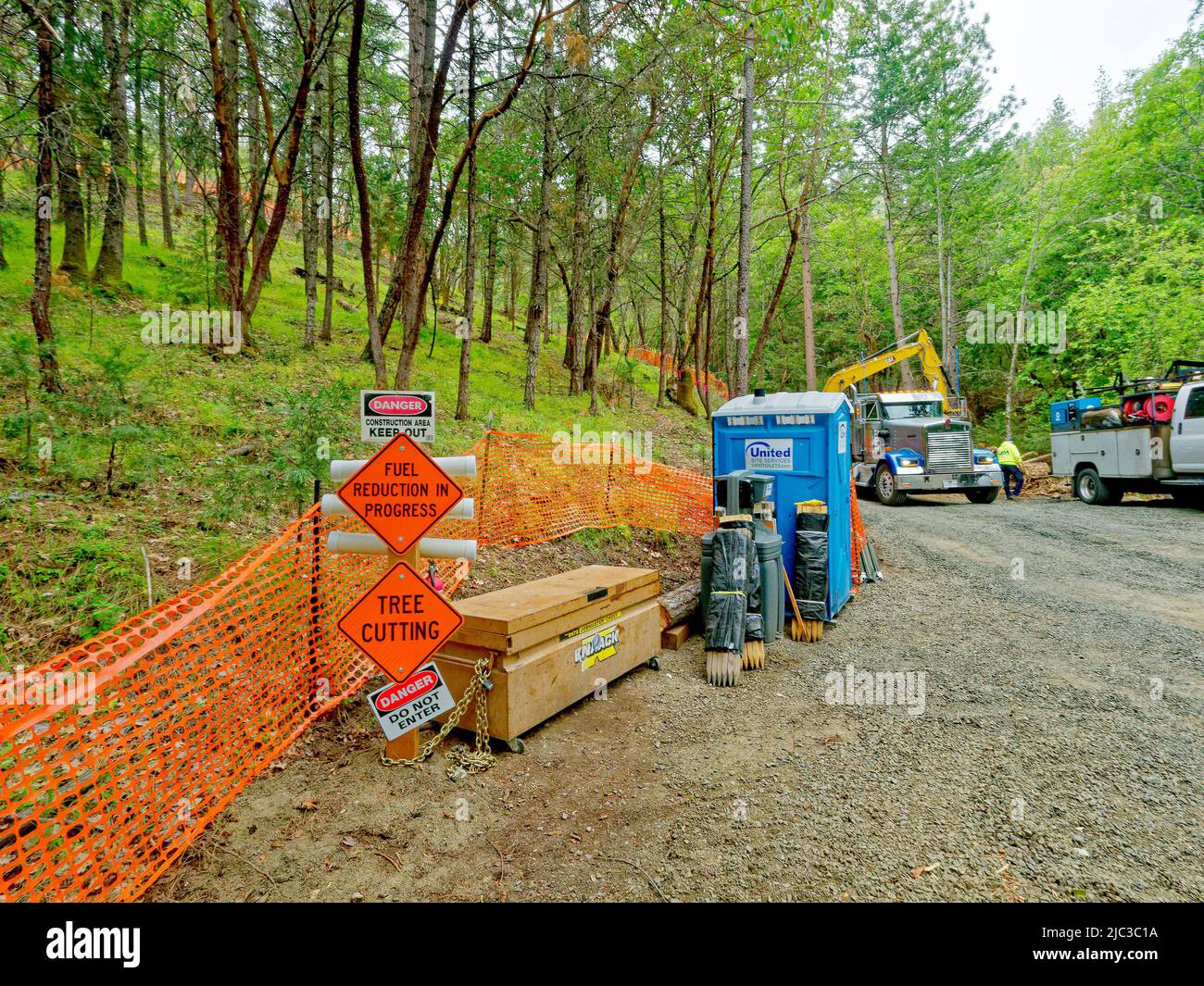 On the hillside above Ashland, Oregon, USA,a sign reads 'fuel reduction in progress' as a crew removes flammable tree lines & shrbs underneath flammable trees. Stock Photo