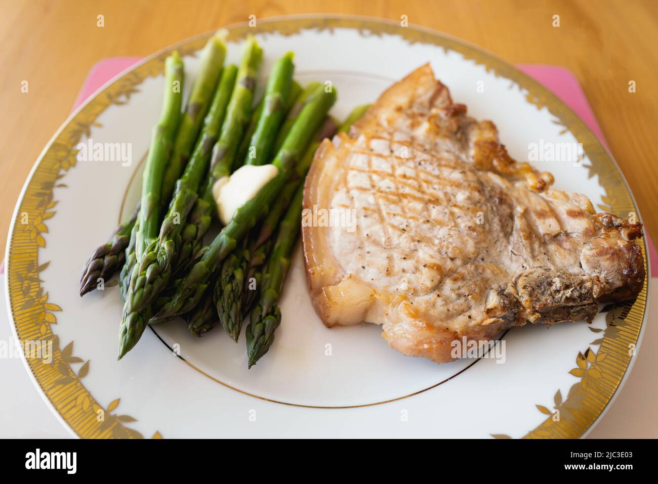 Pork chop and asparagus served with butter on a white plate with a gold trim. Stock Photo