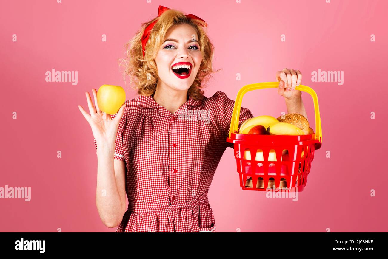 Happy woman with shopping basket full of groceries hold apple. Supermarket or store. Sale. Discount. Stock Photo