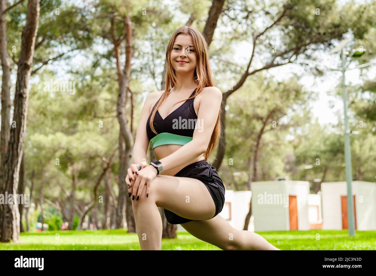 Happy sportive woman wearing sports bra standing on city park, outdoors doing stretching workout. Stretching and motivation, outdoor sport concepts. Stock Photo