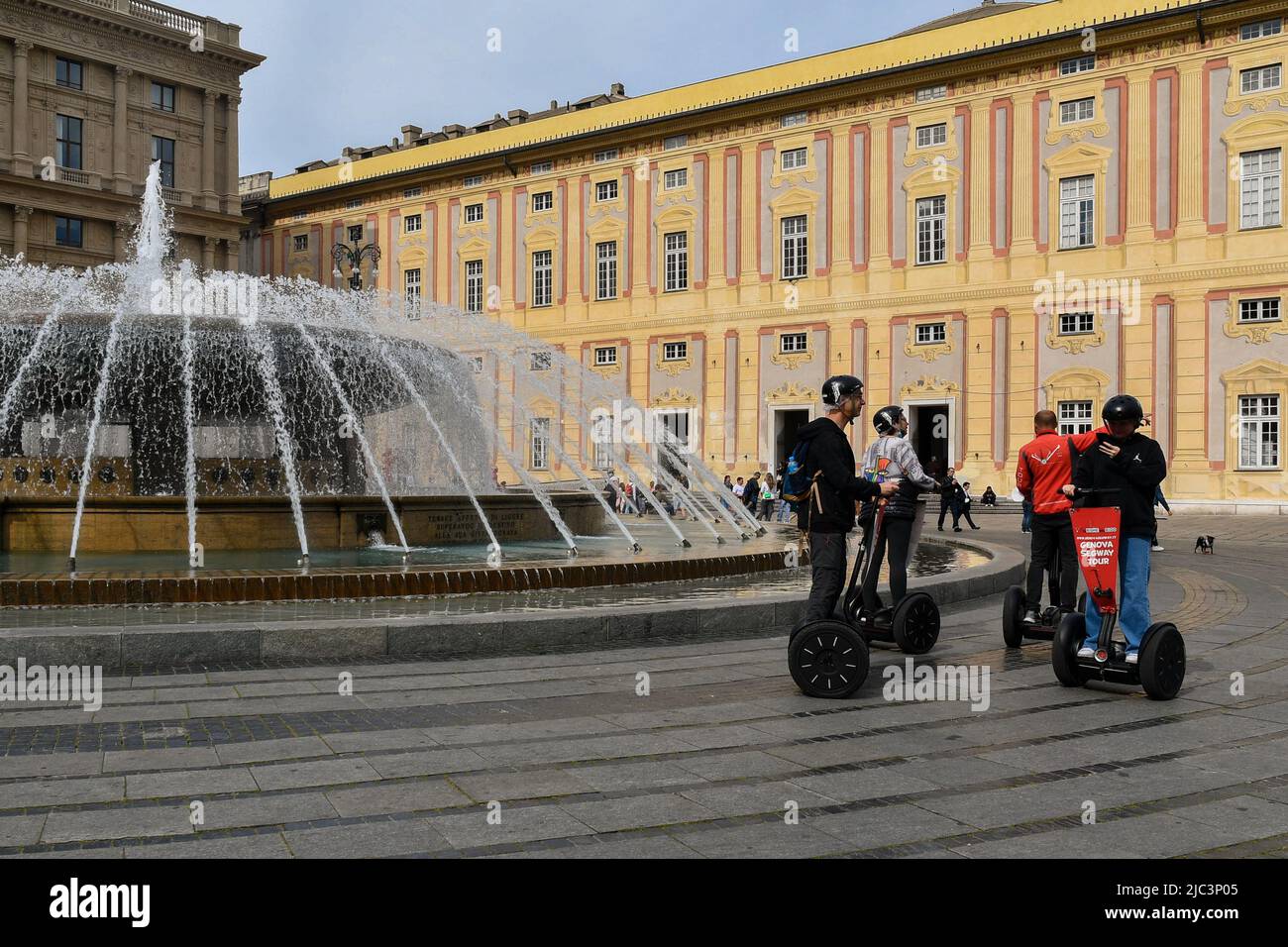 Tourists riding Segway electric vehicles next to the fountain in Piazza De Ferrari square with the Doge's Palace in the background, Genoa, Liguria Stock Photo