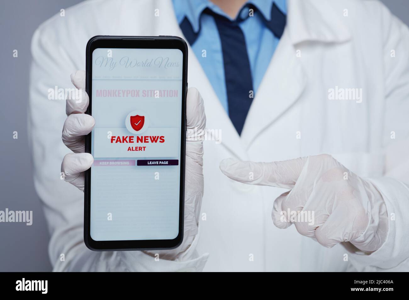 Closeup on modern female medical doctor in white medical robe showing smartphone with monkeypox fake news warning isolated on grey. Stock Photo