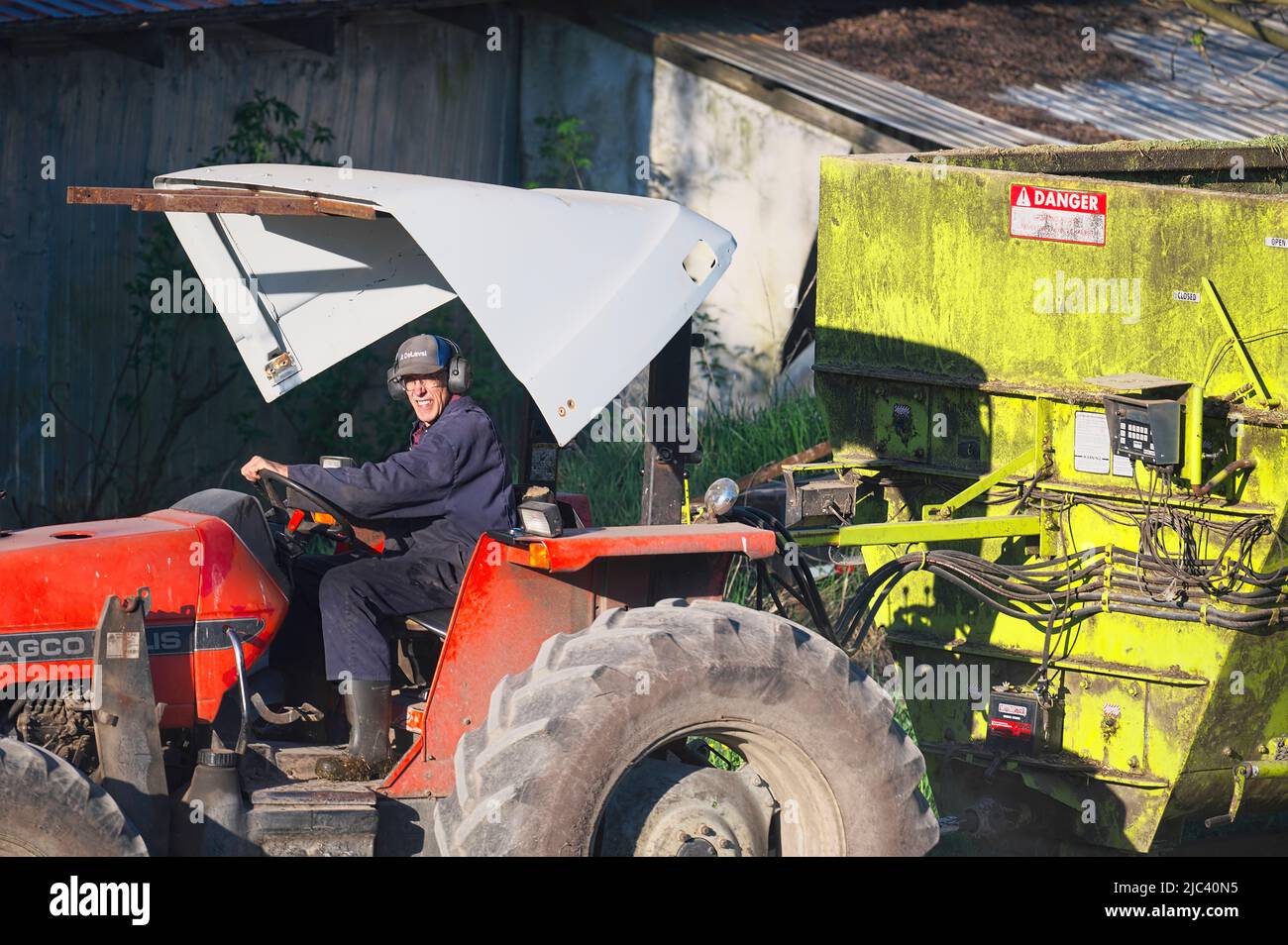 Farmer on tractor wearing headphones in front of a farm building. Stock Photo