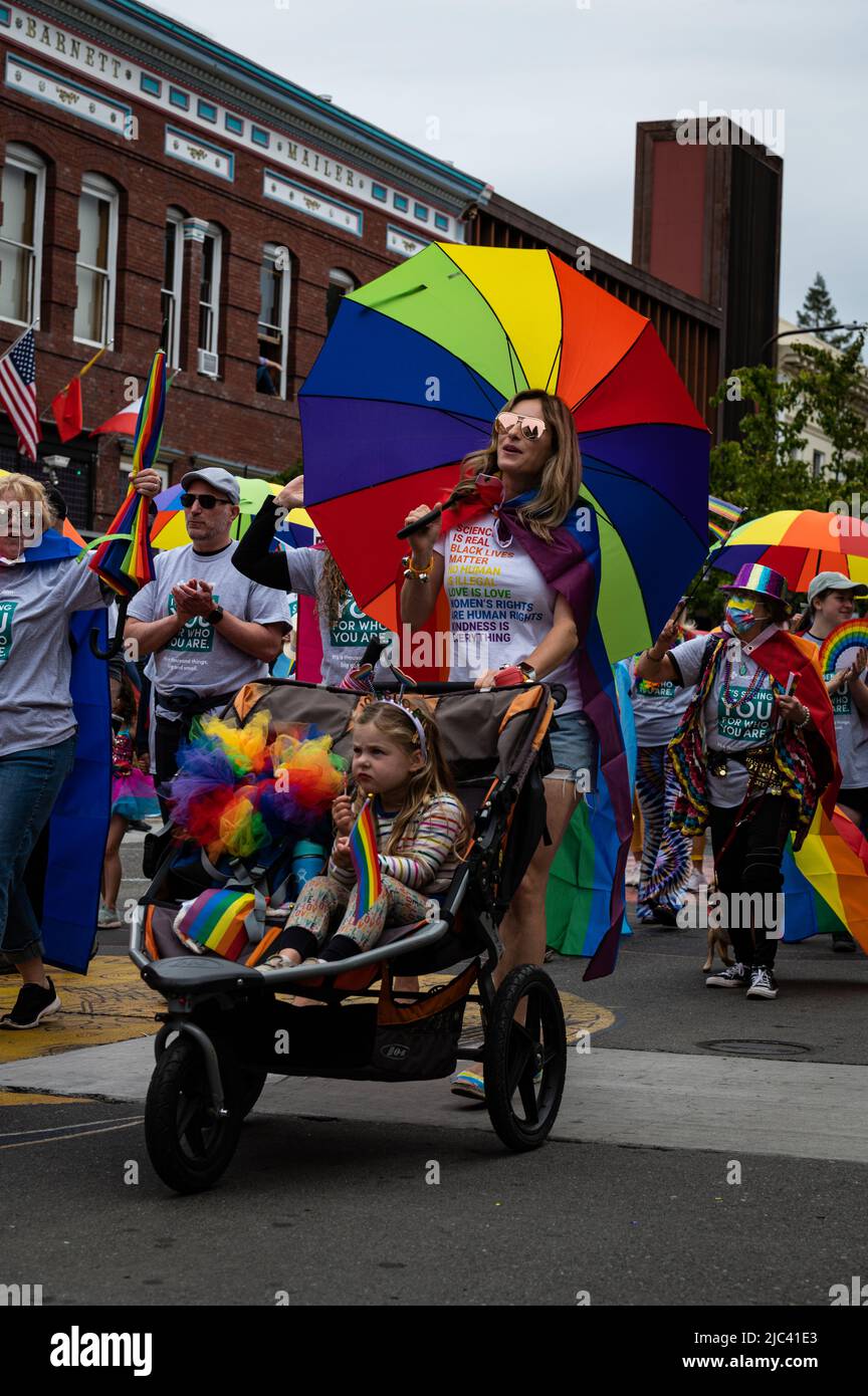 Photo of a Sonoma County Pride parade marcher with sunglasses, rainbow umbrella and child in a stroller. Stock Photo