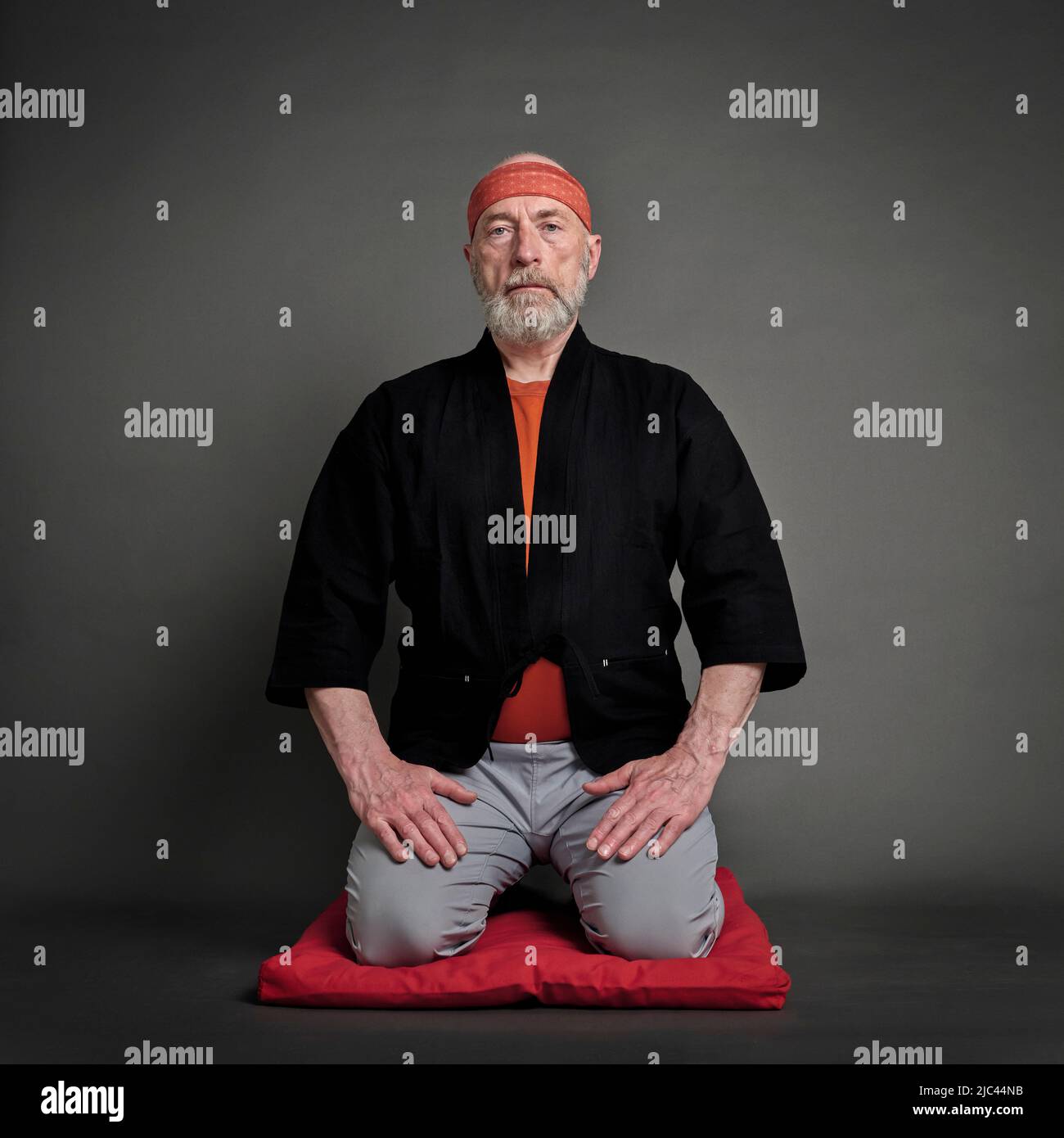 Head and shoulders portrait of bald and bearded senior man wearing a short kimono and sitting in a traditional Japanese seiza position on a cushion pa Stock Photo