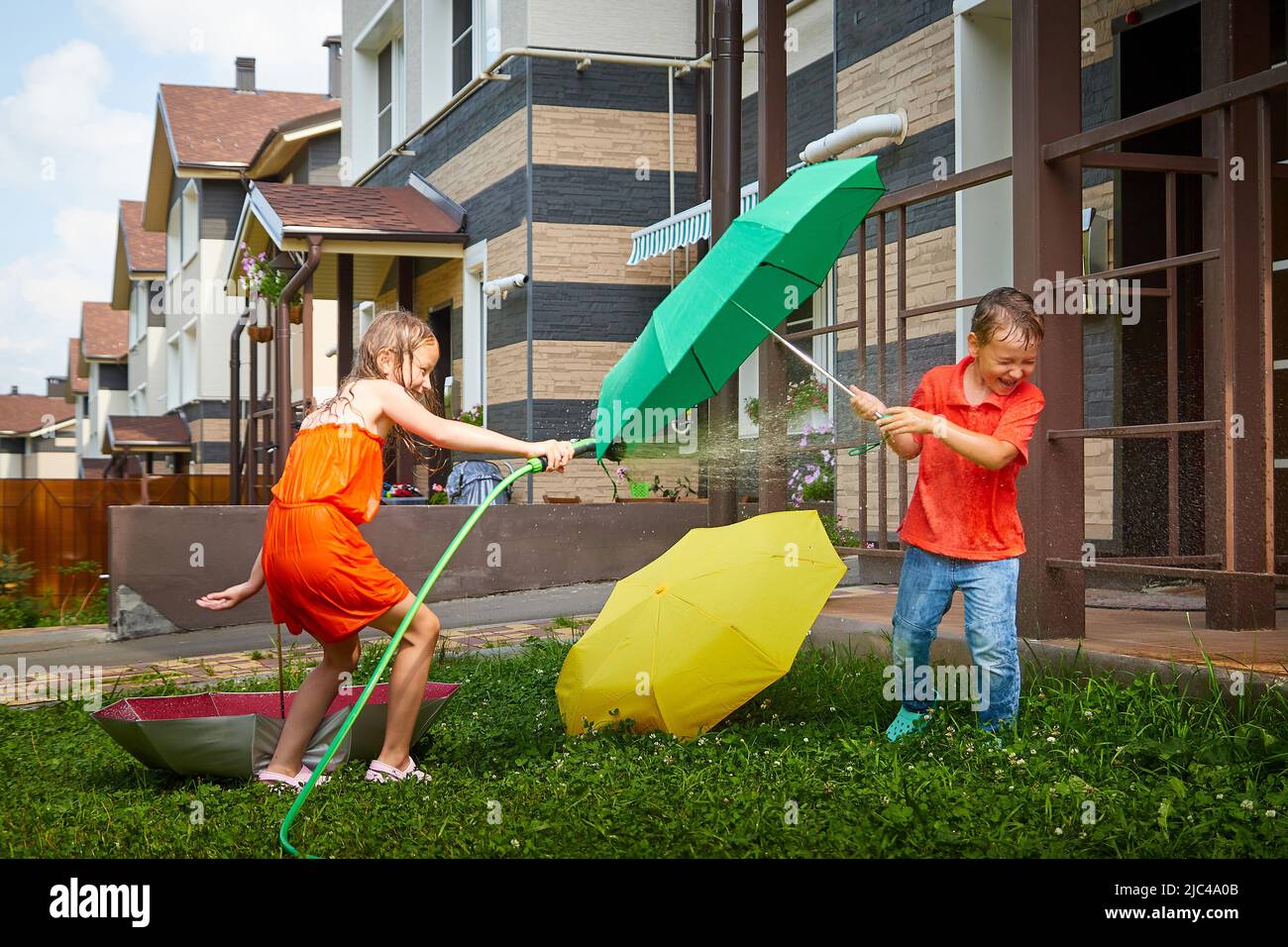 Children playing with garden sprinkler. Brother and sister running and jumping. Summer outdoor water fun in backyard. Boy and girl play with hose Stock Photo