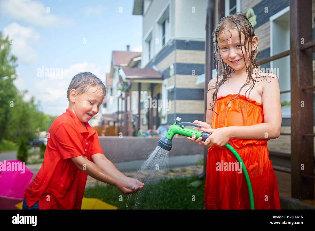 Children playing with garden sprinkler. Brother and sister running and jumping. Summer outdoor water fun in backyard. Boy and girl play with hose Stock Photo