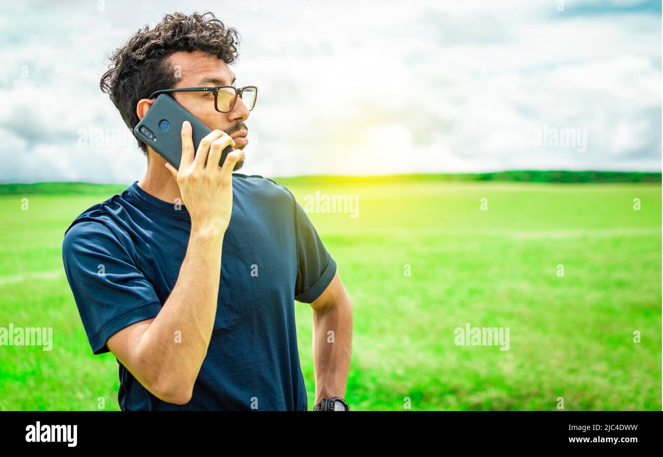 Person with his cell phone in the field calling on the phone, Man calling on the phone in the field, man on a road talking on the phone, young person Stock Photo