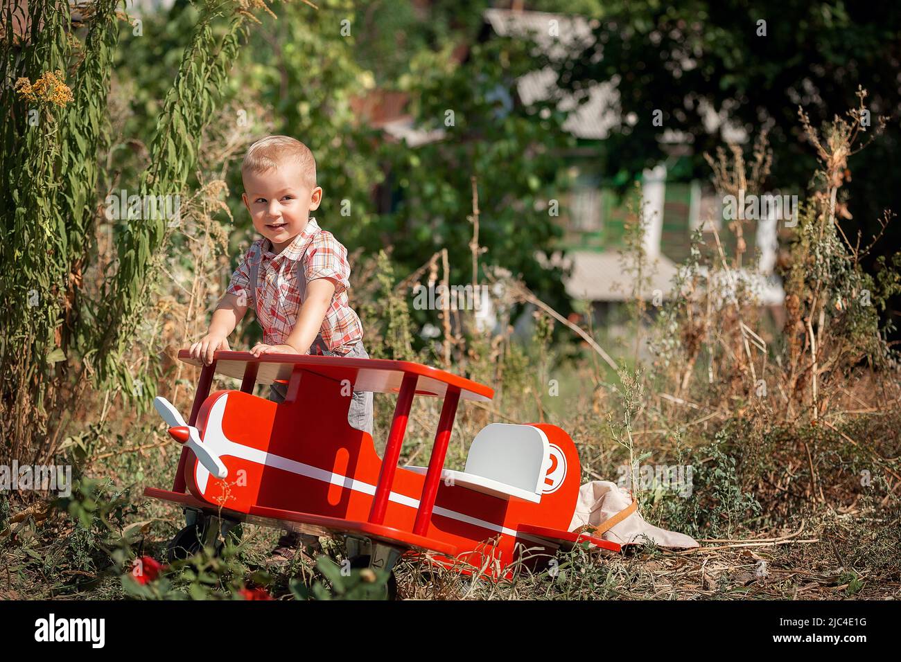 Happy kid boy pilot sitting and playing with toy red airplane on summer ...