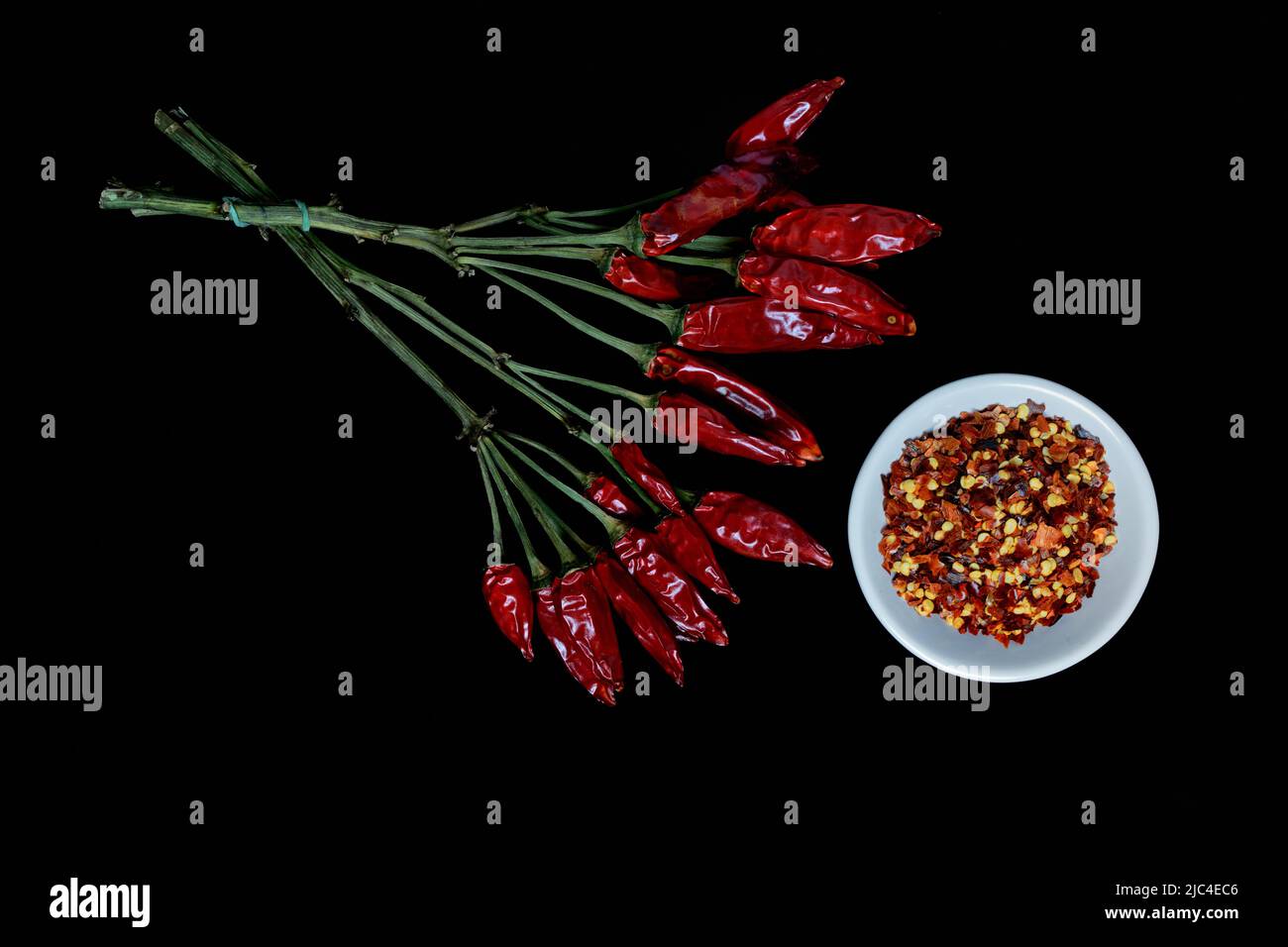 Dried chilli peppers (Capsicum annuum) in bunch and chilli flakes in bowl Stock Photo
