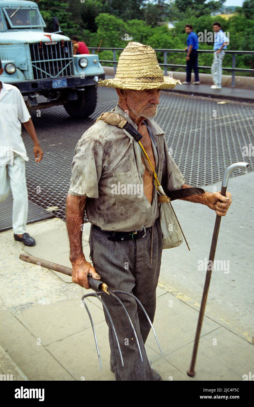 Elderly farmer with dungfork and walking stick on the way to work, Pinar del Rio, Cuba, Caribbean Stock Photo
